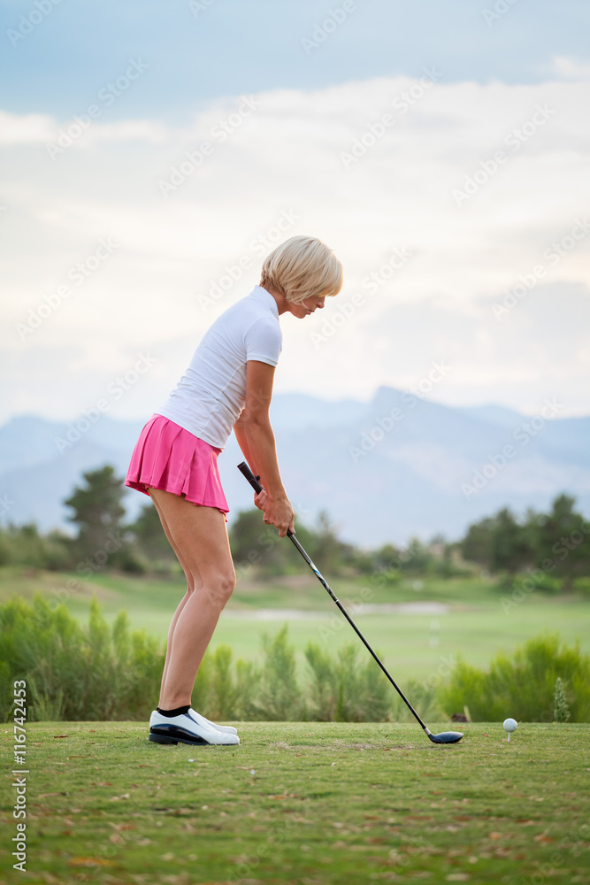 Fototapeta premium Blonde female golfer swinging club on golf course green with cop