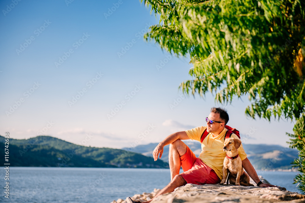 Man and dog sitting on a stone dock  by the sea
