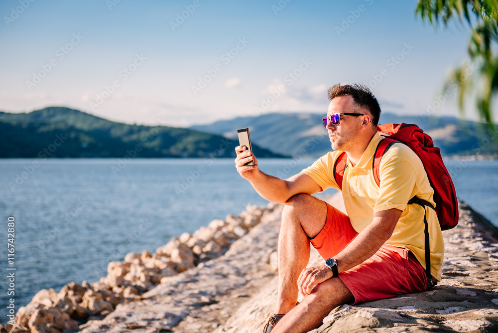 Man sitting by the sea and taking pictures with smart phone Man sitting by the sea and taking pictures with smart phone