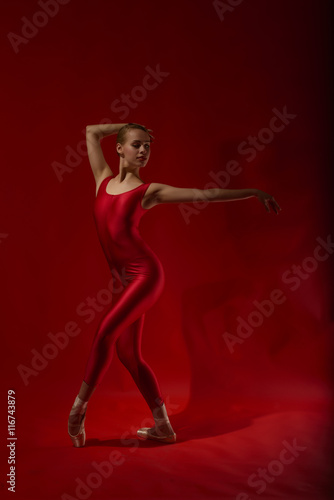 Ballerina in red outfit posing on toes, studio shot on red background. Young beautiful dancer posing in studio © beatricemihaela