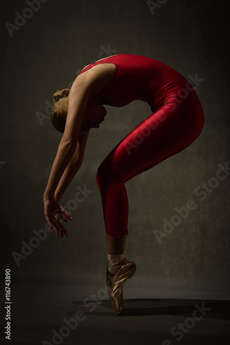 Ballerina in red outfit posing on toes, studio shot on gray background