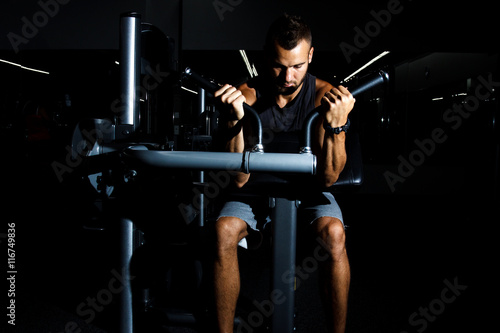 Closeup of a muscular young man lifting weights on dark backgrou