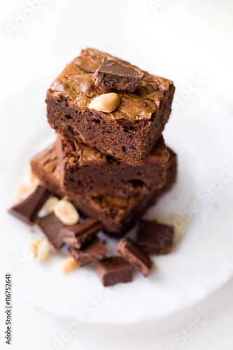 Brownies with nuts and dark chocolate stacked on white dessert plate. Chocolate bars with nuts. Selective focus