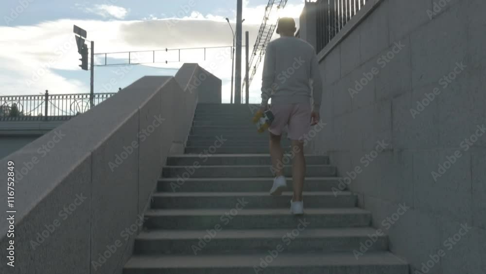 The skateboarder goes up the stairs on the street with a skateboard in hand. The skateboarder goes up the stairs on the street with a skateboard in hand.