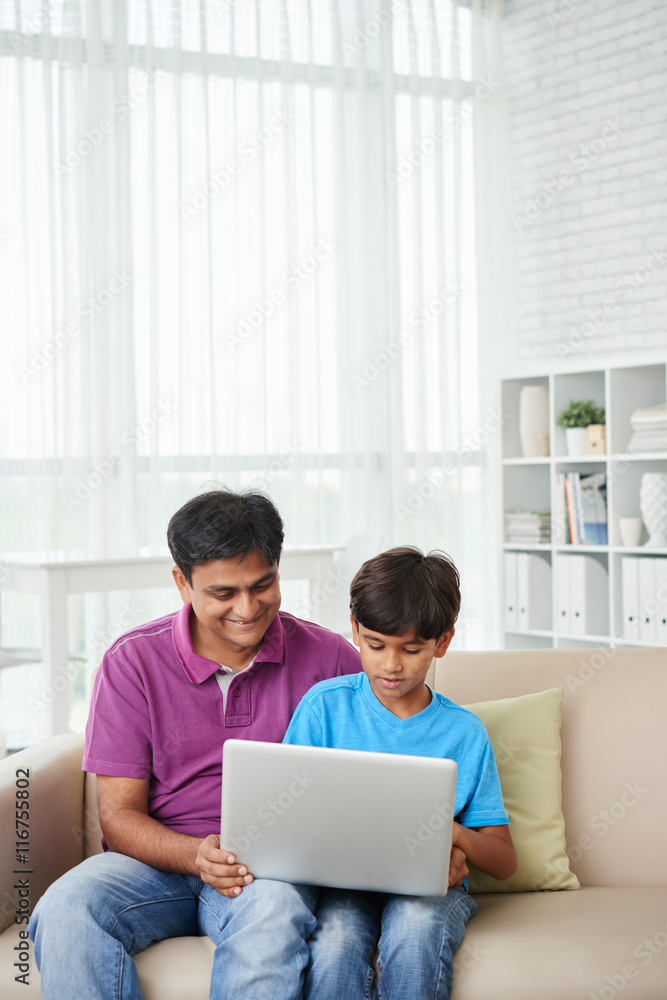 Indian father and child watching movie on laptop together Indian father and child watching movie on laptop together