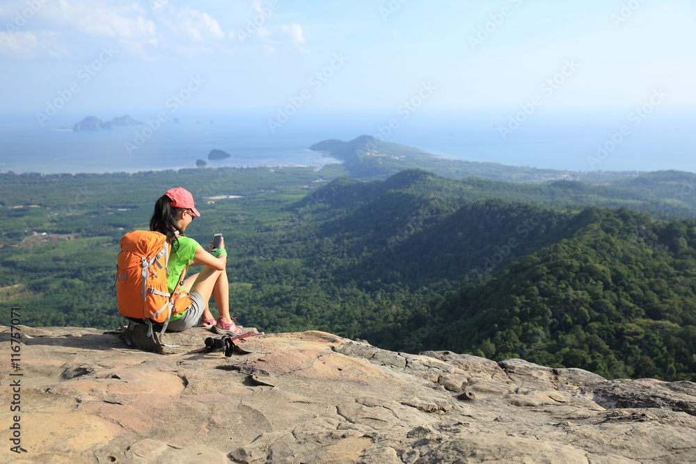 young woman backpacker use cellphone on mountain peak rock