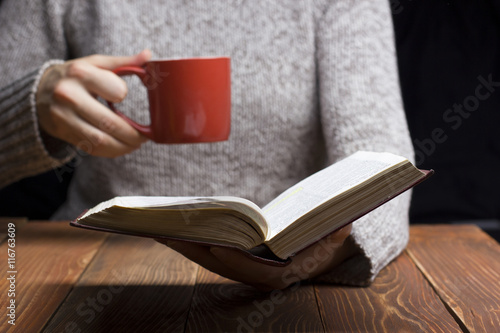 Young woman reading a book and holding cup of tea or coffee. Toned image