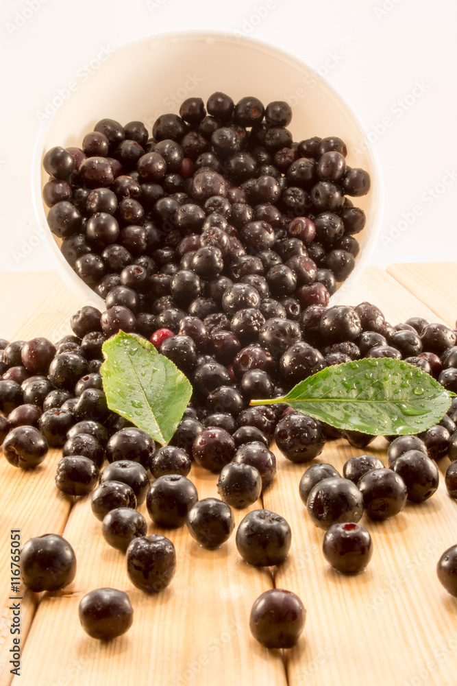 Bowl full of aronia spilled on wooden table Bowl full of aronia spilled on wooden table