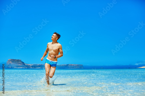 strong athletic man with bared torso running on the beach along the sea front