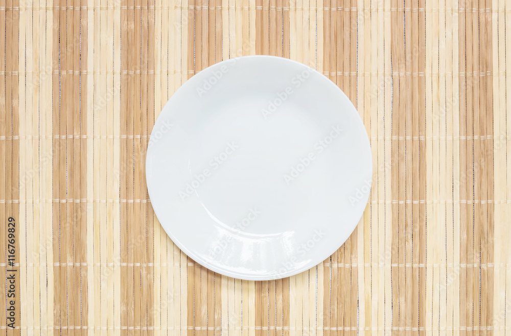 Closeup white ceramic dish on wood mat textured background at the center on dining table in top view with copy space Closeup white ceramic dish on wood mat textured background at the center on dining table in top view with copy space