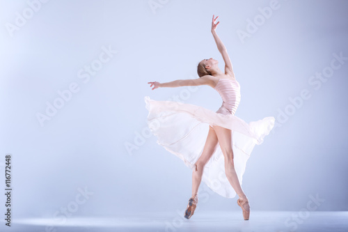 Fototapeta Naklejka Na Ścianę i Meble -  Ballet Perfection. Young and beautiful ballerina in a white dress is posing in a white studio full of light.
