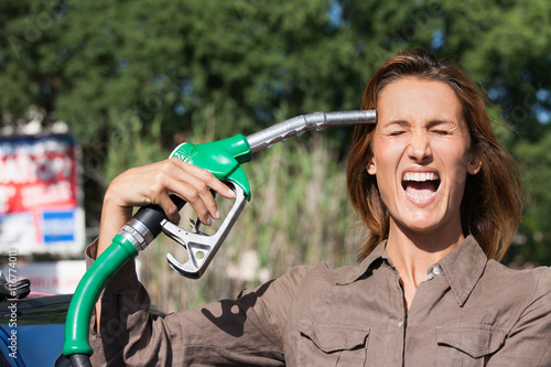 Fotografie femme qui crie dans une station essence avec le pistolet sur la tempe