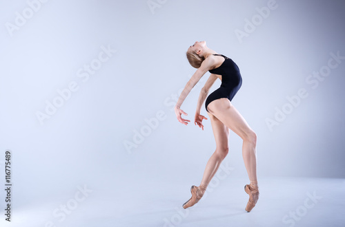Ballet Perfection. Young and beautiful ballerina in a black dancing suit is posing in a white studio full of light.