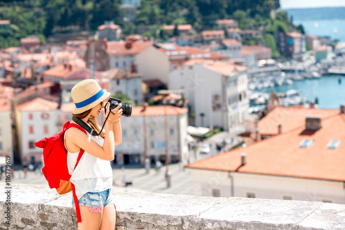 Fotografie Young female traveler with red backpack photographing with photo camera Piran old town