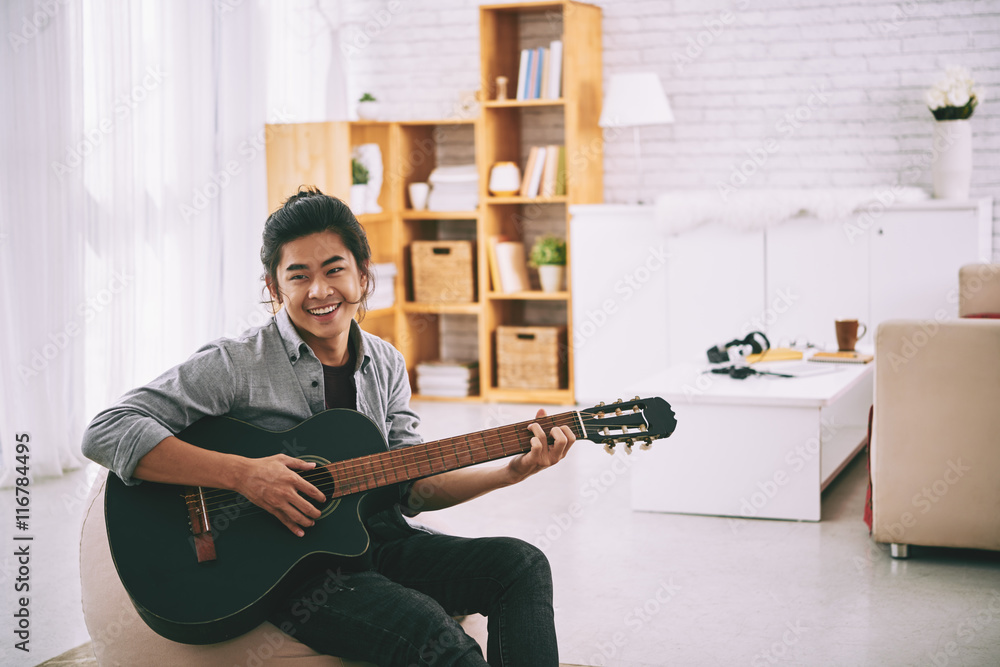 Portrait of young Vietnamese man practicing playing guitar at home