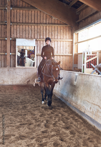 Young woman rider walking her horse indoors