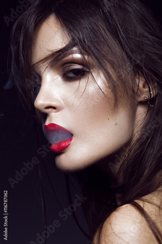 Beautiful sexy brunette girl with bright makeup, red lips, smoke from mouth. beauty face.