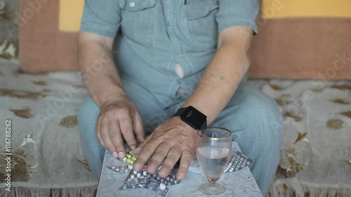 Senior man chooses the desired a pill from the set. It takes one pill, and drinks water. Close up