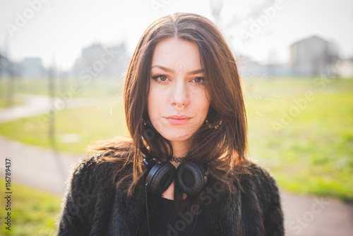 Portrait of young beautiful caucasian indie woman with septum piercing posing outdoor in city back light looking in camera, serious - thoughtful, peaceful, thinking future concept