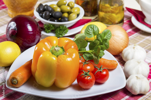 Fresh  orange bell pepper  basil  cherry tomatoes and carrot served on a plate  next to the bowl with green and black olives  onion  garlic - vegetable  herb  curative  vegan food.