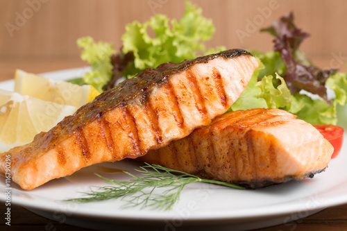 Grill salmon steak serve with lemon and colorful salad on wooden table