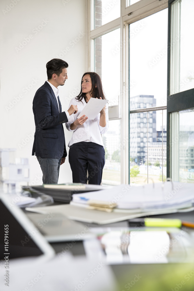 Businessman and woman standing at office window, talking Businessman and woman standing at office window, talking