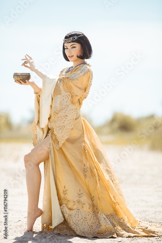 Beautiful woman like Egyptian Queen Cleopatra with cup outdoor in desert