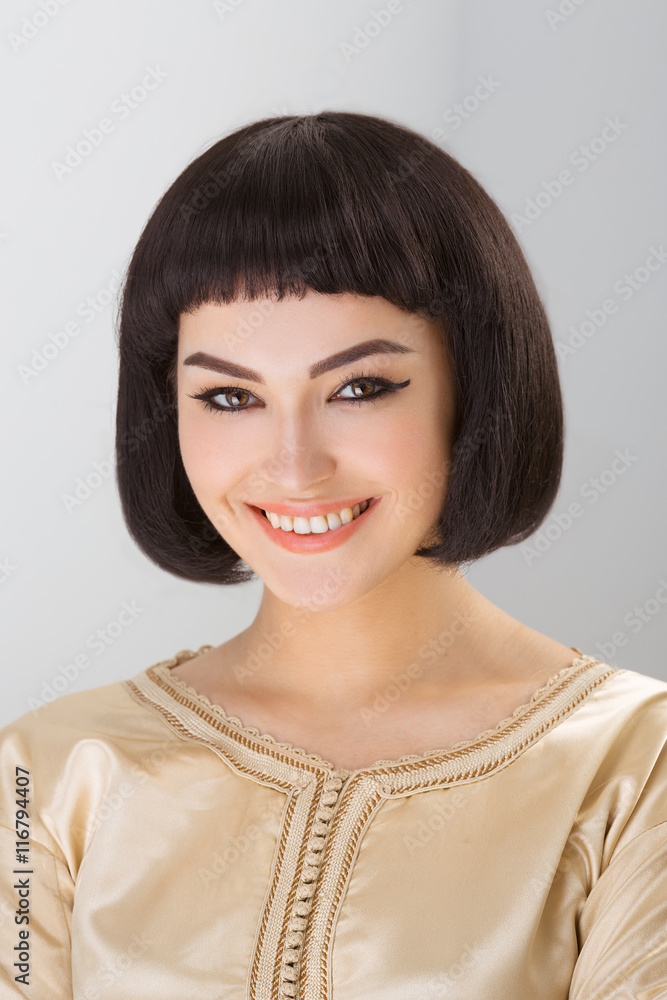 Smiling girl with Cleopatra's make-up and haircut posing in studio