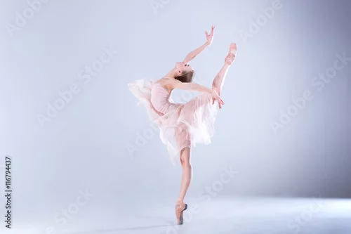 Obraz Doskonałość baletowa. Młoda i piękna baletnica w białej sukni pozuje w białym studiu pełnym światła.