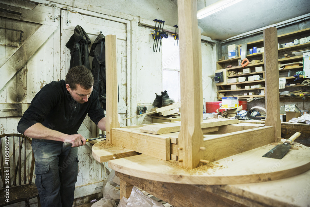 A man in a carpentry workshop, working on the edge of a new wooden table using a hammer. A man in a carpentry workshop, working on the edge of a new wooden table using a hammer.