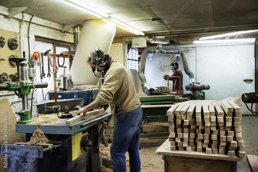 Man standing in a carpentry workshop, wearing a respirator and hearing protector, working on a piece of wood. Man standing in a carpentry workshop, wearing a respirator and hearing protector, working on a piece of wood.