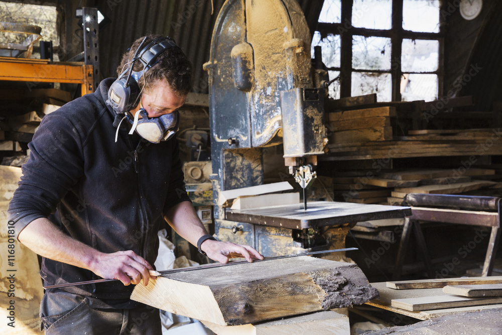 Man working in a carpentry workshop, wearing a respirator and hearing protector, measuring a plank of wood. Man working in a carpentry workshop, wearing a respirator and hearing protector, measuring a plank of wood.