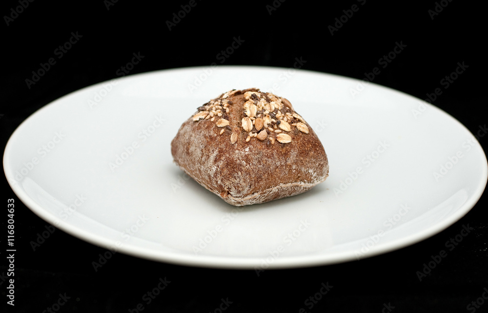 Rye sandwich bun with cereals on white plate 