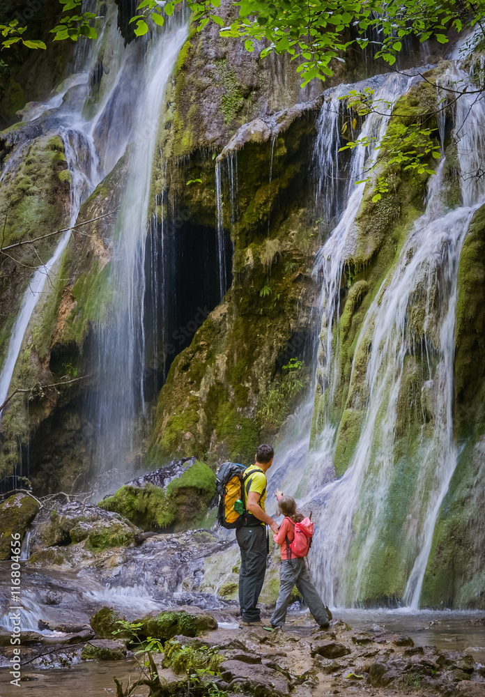 Father and daughter close to a waterfall in a forest