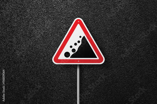 Road sign triangular shape with a picture of the rockfall on a background of asphalt. The texture of the tarmac, top view. © srzaitsev