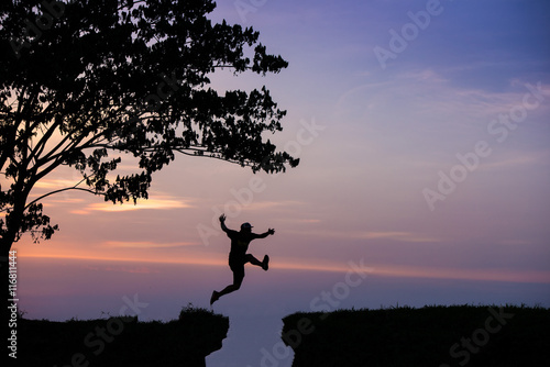 Foto Silhouette of man jumping over cliff on sunset background , business concept
