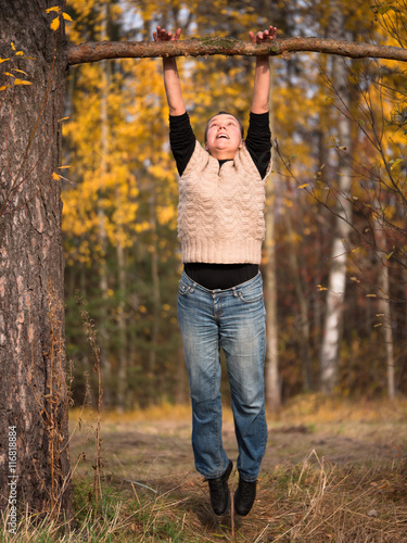 A woman in a sweater and jeans pulled to a branch on blurred background