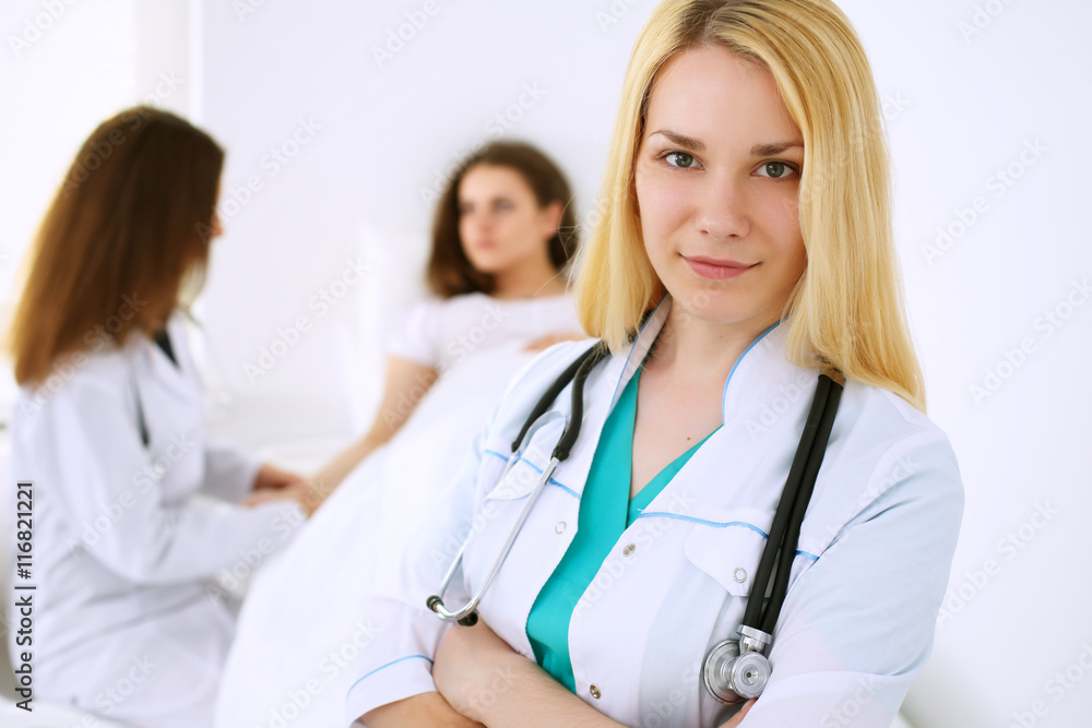 Young beautiful female doctor smiling on the background with patient and his physician in hospital. High level and quality medical service concept. Young beautiful female doctor smiling on the background with patient and his physician in hospital. High level and quality medical service concept.
