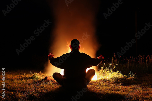 Silhouette of a man sitting in the lotus position at night by th