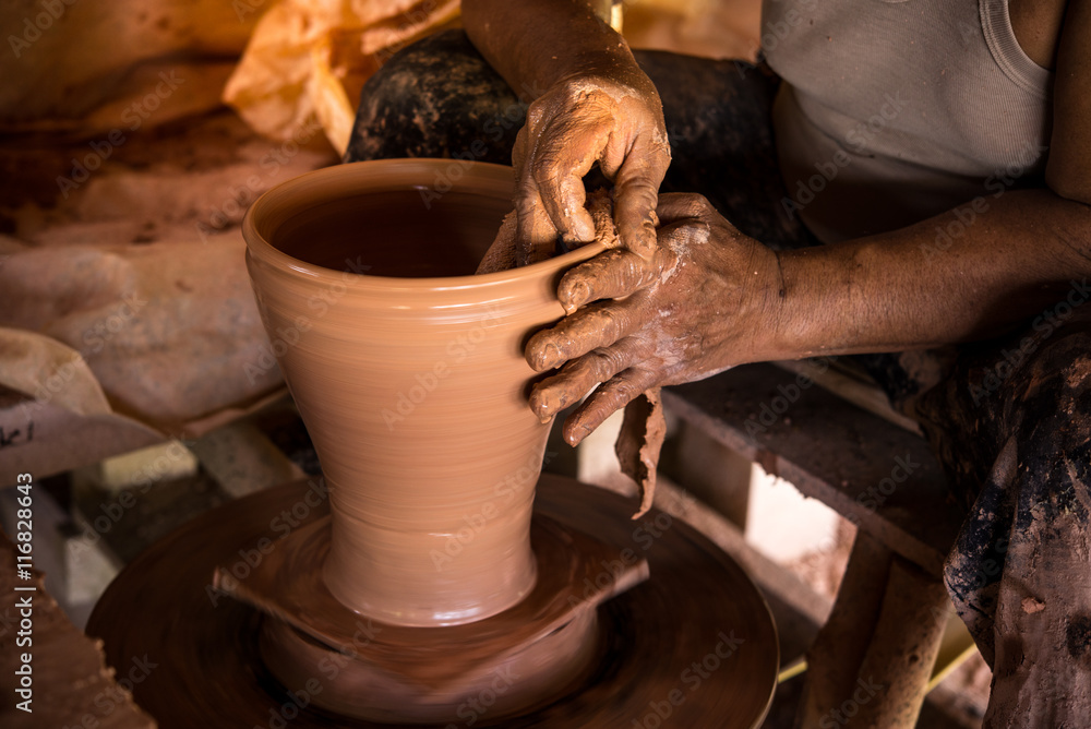 Old potter creating a new ceramic pot on pottery wheel