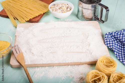 Sprinkled flour on wooden cutting board, pasta, millet and blue napkin