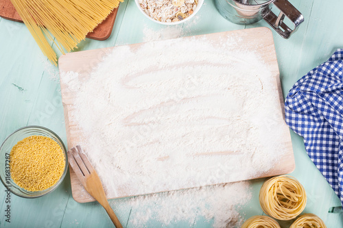 Sprinkled flour on wooden cutting board, pasta, millet and blue napkin