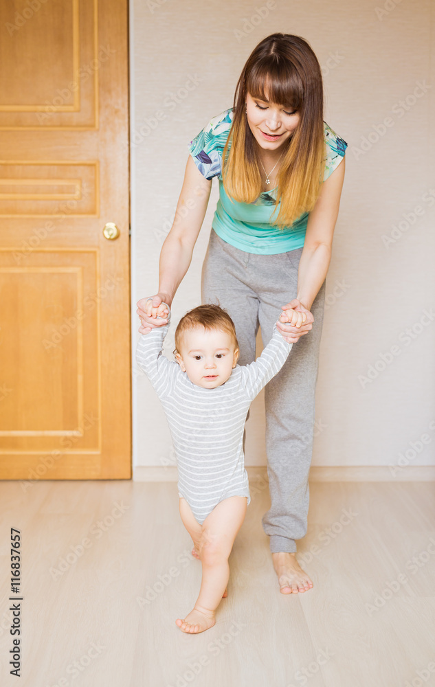 Mother teaching her cute little son to walk holding hands body part first baby steps concept Mother teaching her cute little son to walk holding hands body part first baby steps concept