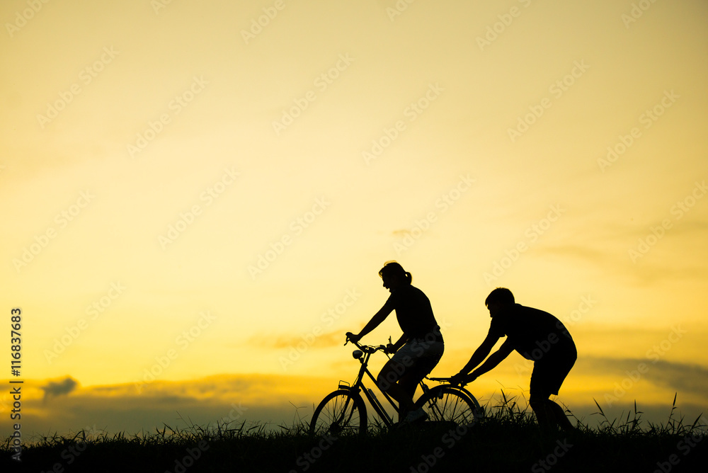 sillhouette of man teaching woman to ride bicycle with vintage bicycle at sunset time.