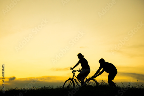 sillhouette of man teaching woman to ride bicycle with vintage bicycle at sunset time.