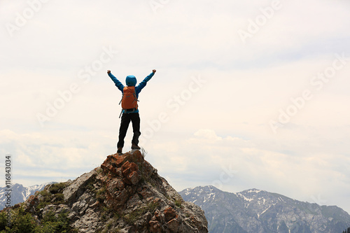 cheering successful woman backpacker open arms on mountain peak