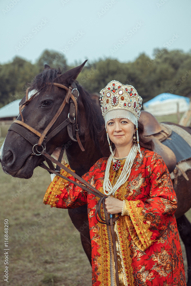 Medieval noblewoman in red dress and jewelry is going to a horse