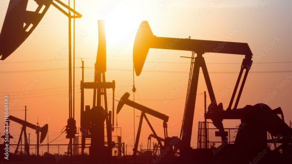 The sun rises behind a large oil field. The sun rises behind a large oil field.