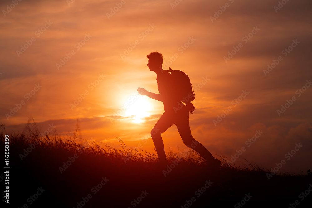 Silhouette of tourist man spread hand on top of a mountain enjoying sunset