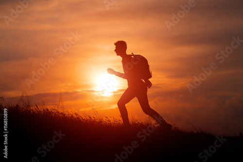 Silhouette of tourist man spread hand on top of a mountain enjoying sunset
